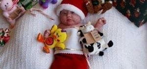 Baby in a Santa hat and stocking surrounded by Christmas toys.