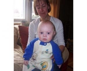 A woman holds a baby wearing a blue and white outfit with cartoon characters.