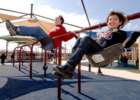 Two children laugh as they swing at Morgan's Wonderland, an accessible family fun park.