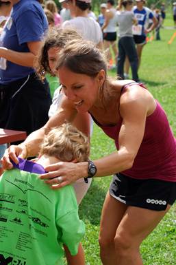 Woman congratulates child in green shirt with purple collar at an outdoor event.