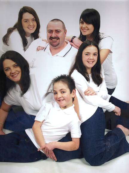 A family poses for a portrait, with a man and four children in white shirts and jeans.