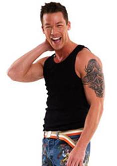 Man in a black tank top and jeans smiles with his hand on his neck.