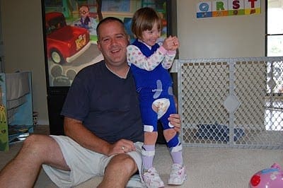 A man sits on the floor holding a young girl dressed in blue pajamas.