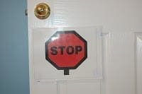 A stop sign is taped to a white door with a brass doorknob.