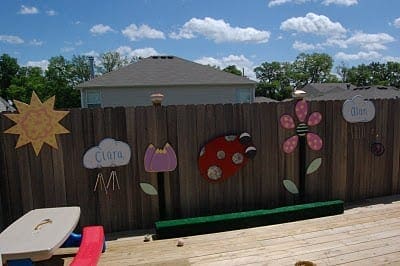 Wooden fence decorated with colorful cutouts of a sun, clouds, flowers, and a ladybug.