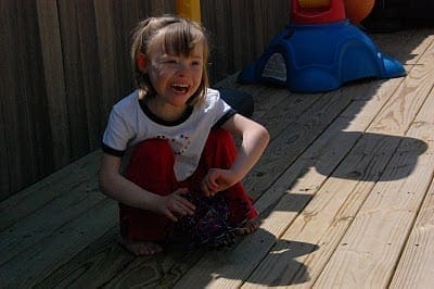 Child with face markings sits on a wooden deck outside, crying.
