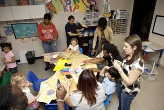 Adults and children gather around a table in a classroom setting, working on a project together.