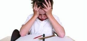 Boy with hands on head looking distressed at a desk.