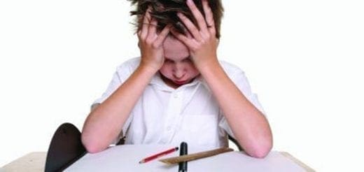 Boy with hands on head looking distressed at a desk.