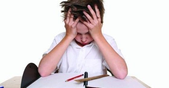 Child with head in hands at a desk with schoolwork.