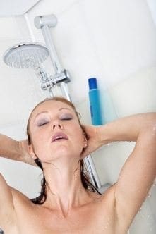 Woman with eyes closed in shower, hands behind her head.
