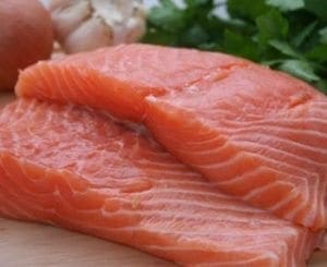 Raw salmon fillets with garlic and parsley in the background.