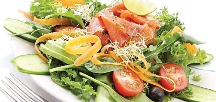 Salmon salad with cucumber, tomatoes, and greens on a white plate.