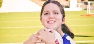 Lucy Meyer holding a soccer ball and smiling on a soccer field.
