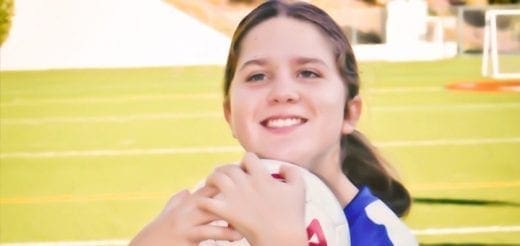 Lucy Meyer holding a soccer ball and smiling on a soccer field.