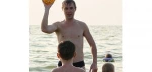 Man holding a ball with two children in the water.