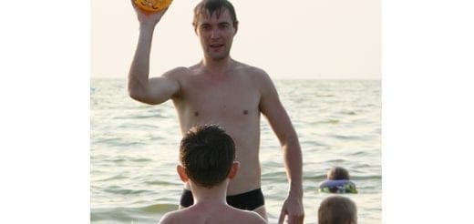 Man holding a ball with two children in the water.