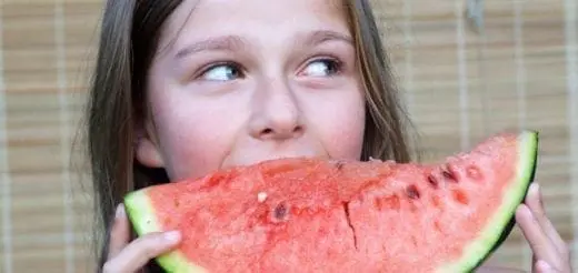 A young girl eats a slice of watermelon.