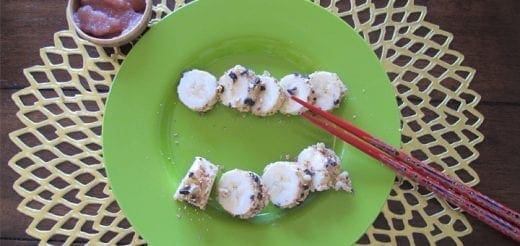 Banana sushi with chocolate chips on a green plate.