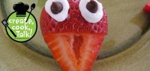Strawberry decorated to look like a head with frosting and chocolate chip eyes.