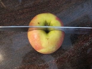 Knife cutting an apple in half on a counter.
