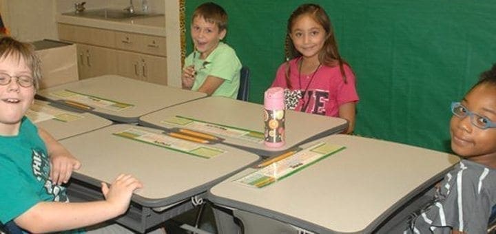 Four children sit at desks in a classroom.