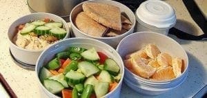 Four round containers filled with lunch food: a salad, sandwiches, and fruit slices.