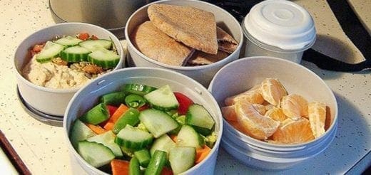 Four round containers filled with lunch food: a salad, sandwiches, and fruit slices.
