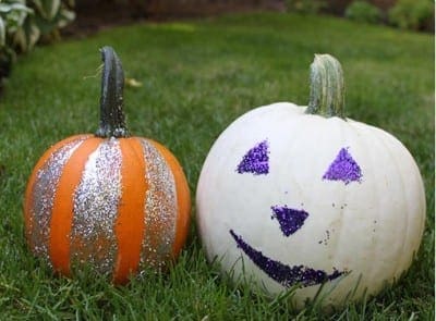 Two pumpkins decorated with glitter and paint sit on grass.