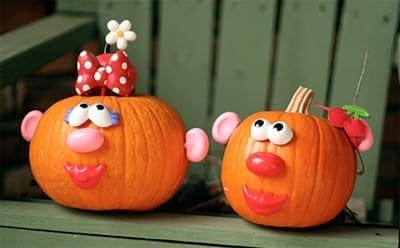 Two pumpkins decorated to resemble Mr. and Mrs. Potato Head with attached eyes, noses, mouths, and ears.