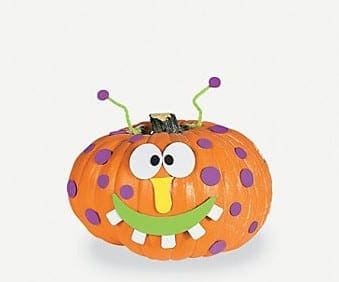 Orange pumpkin decorated as a monster with purple polka dots, googly eyes, a yellow nose, and a green smiling mouth.