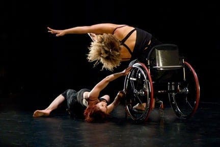 Dancers with and without disabilities perform onstage with a wheelchair.