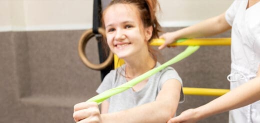 Young girl smiling while exercising with a resistance band and physical therapist.