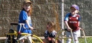 Three children with adaptive mobility equipment stand outside.