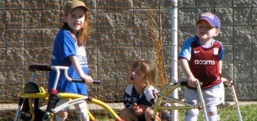 Three children with adaptive mobility equipment stand outside.