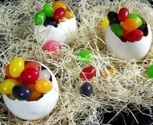 Easter eggs filled with colorful jelly beans sit on a bed of straw.