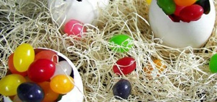 Easter eggs filled with colorful jelly beans sit on a bed of straw.