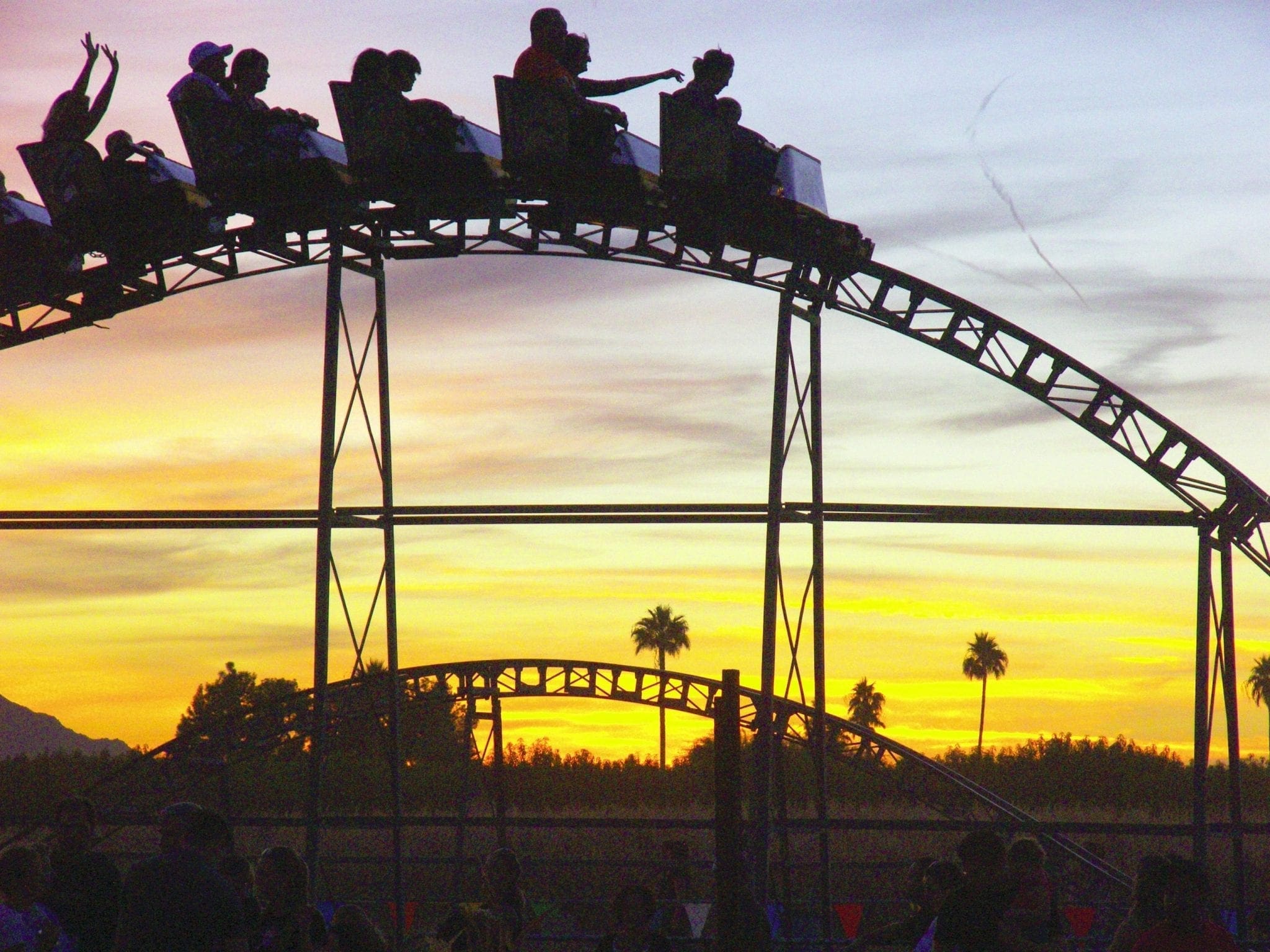 Silhouettes of people on a roller coaster against a sunset sky.