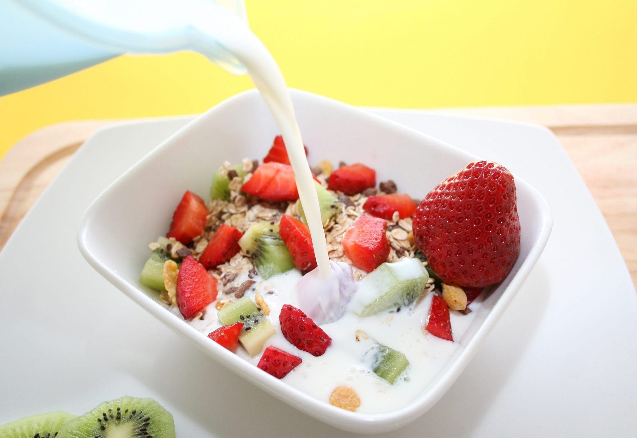 Milk being poured into a bowl of oatmeal with strawberries and kiwi.