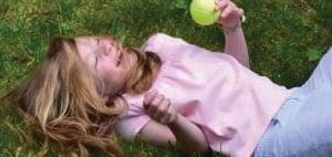 Andrea lies on the grass holding a yellow ball.