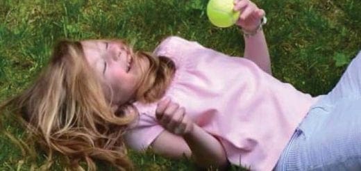 Andrea lies on the grass holding a yellow ball.