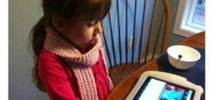 Young girl wearing a pink scarf and red sweater looks at a tablet.