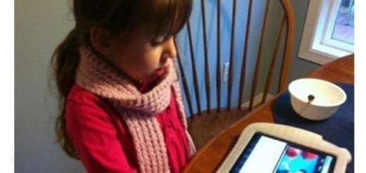 Young girl wearing a pink scarf and red sweater looks at a tablet.
