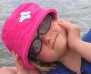 Young girl wearing a pink bucket hat and sunglasses tilts her head back.