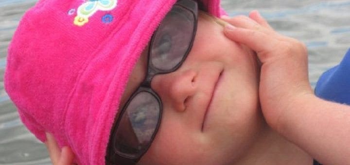 Young girl wearing a pink bucket hat and sunglasses tilts her head back.