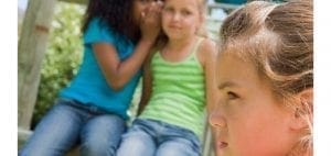 Girl whispering into another girl's ear while a third girl looks away.