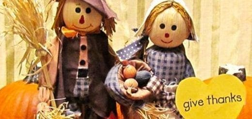 Two scarecrows stand by pumpkins with a yellow heart that says "give thanks.