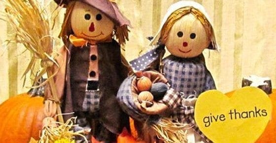 Two scarecrows and pumpkins with a yellow heart that says "give thanks.