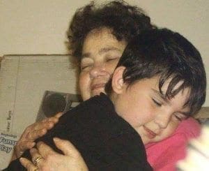 A woman hugs a young boy, both with eyes closed.