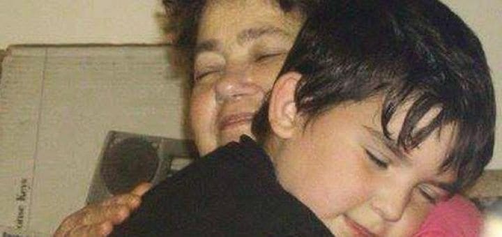 A woman hugs a young boy, both with eyes closed.